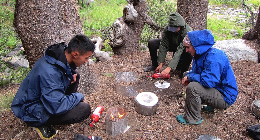 Three outward bound students use camping stoves to prepare food. 